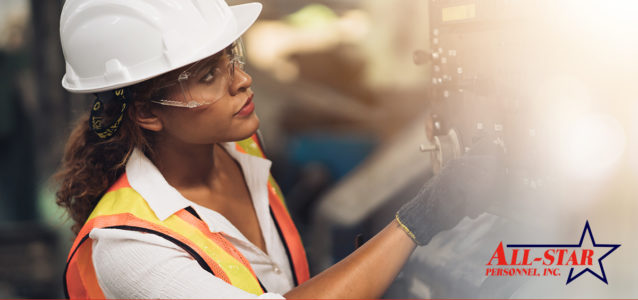 female worker wearing a hardhat and protective glasses is working machinery